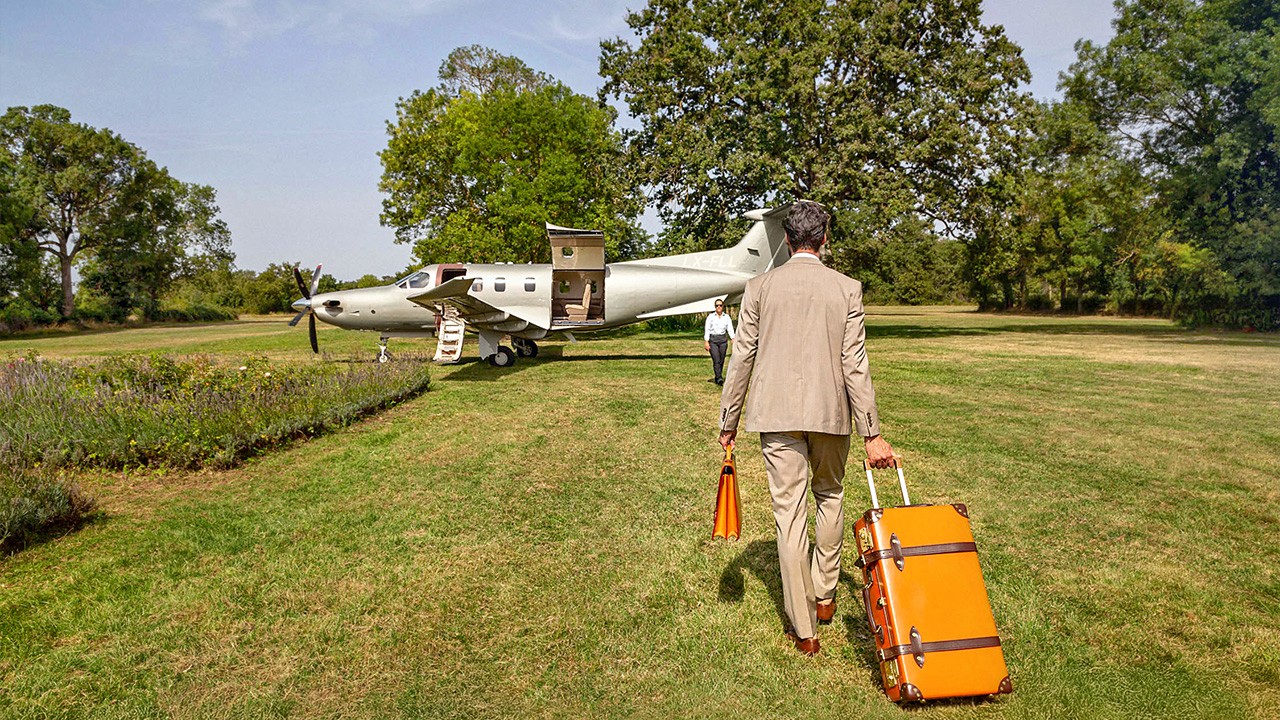 Un homme marchant vers un Pilatus PC-12 de Jetfly sur une piste en herbe